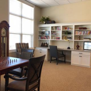 A cozy office with a desk, bookshelf, and a chessboard by the window.