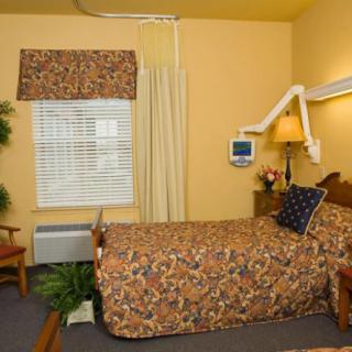 A cozy single-bed hospital room with floral bedding and warm yellow walls.