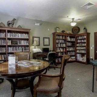 A cozy library room with bookshelves, a computer, a round table, and chairs.