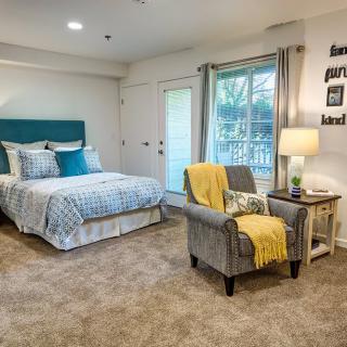 A cozy, modern bedroom with a neatly made bed, an armchair, and stylish decor.