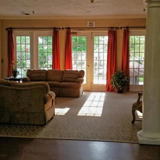 A cozy living room with large windows and red curtains, featuring a comfortable sofa and natural lighting.