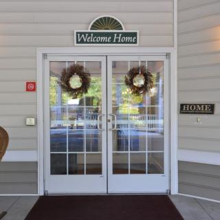 A double glass door entrance adorned with wreaths and a 'Welcome Home' sign above.
