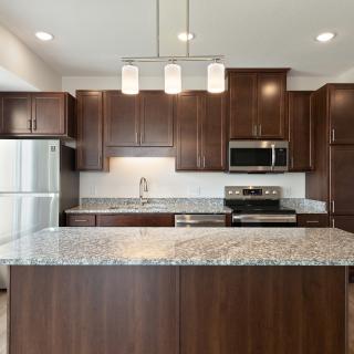 A modern kitchen featuring dark wood cabinetry, granite countertops, and stainless steel appliances.