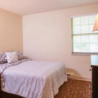 A cozy, well-lit bedroom featuring a double bed, a bedside lamp, and a window that brings in natural light.