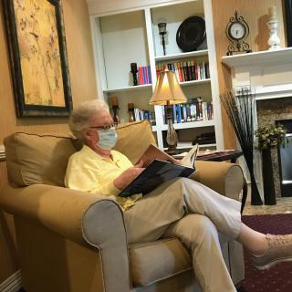 A person wearing a mask is sitting in a chair reading a book in a cozy living room.