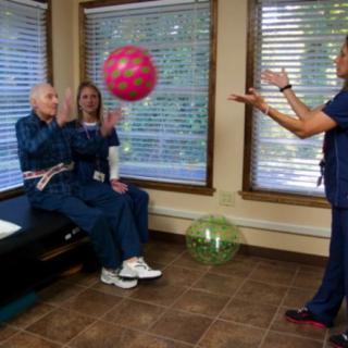 Seniors participating in a physical therapy session with a healthcare professional using therapy balls.
