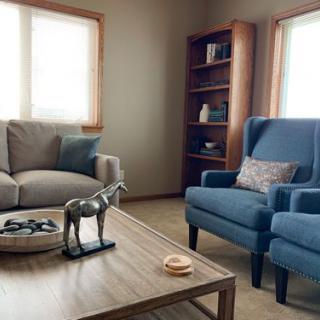 A cozy living room with a sofa, armchair, and coffee table, complemented by bookshelves and natural light.