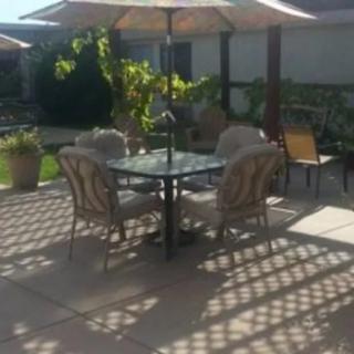 A sunny patio with a table set and umbrella, surrounded by a garden.