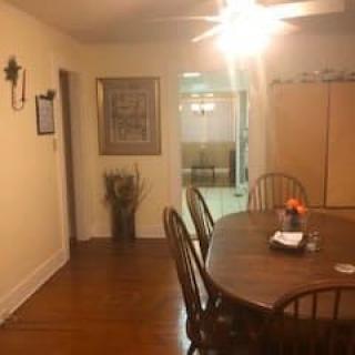 A cozy dining room with a wooden table and chairs, adorned with wall art and lit by a ceiling fan.
