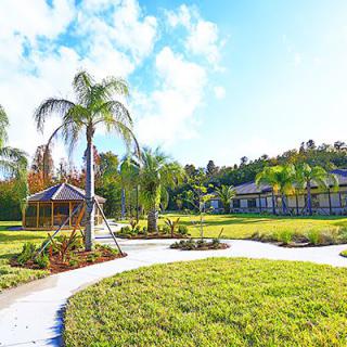 A beautifully landscaped garden with palm trees and a winding pathway leading to a gazebo on a sunny day.