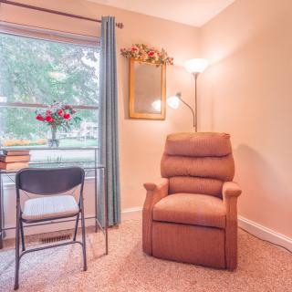 A cozy living room corner featuring a comfortable armchair, a lamp, and soft natural light streaming through the window.