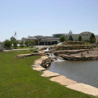 A scenic view of a park featuring a pond and small waterfall surrounded by green grass.
