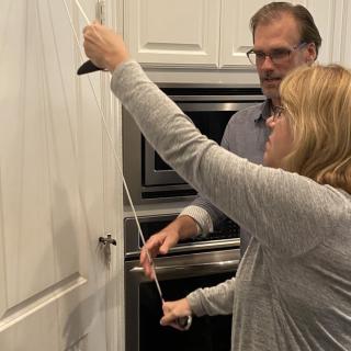 Two people working together to measure a kitchen cabinet with a tape measure.