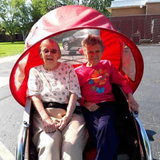 Two elderly individuals enjoying a ride in a bicycle cart outdoors.