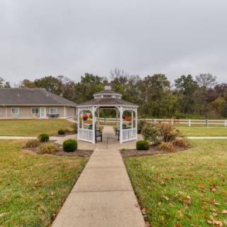 A white gazebo in a garden setting with a pathway leading towards it on an overcast day.