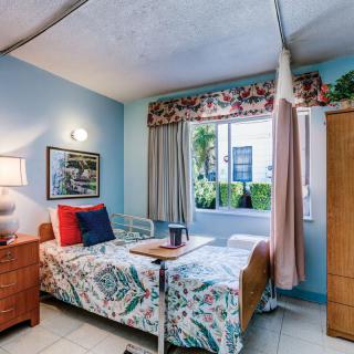 A cozy hospital room with a single bed, bedside table, and a window with floral curtains.