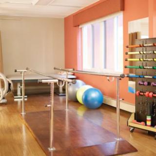 A physical therapy room equipped with parallel bars, therapy balls, and a rack of dumbbells.