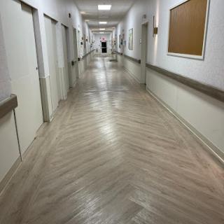 A long, well-lit corridor in a hospital with multiple doors opening to rooms.
