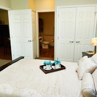 A cozy bedroom featuring a neatly made bed with a tray of cups, leading to a bathroom and closet area.