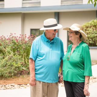 An elderly couple wearing hats and casual clothing, enjoying a walk in the garden.