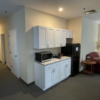 A small kitchen area with white cabinets, a microwave, and a refrigerator in a room.