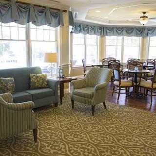 A cozy living area featuring a sofa, chairs, and tables with large windows and decorative curtains.