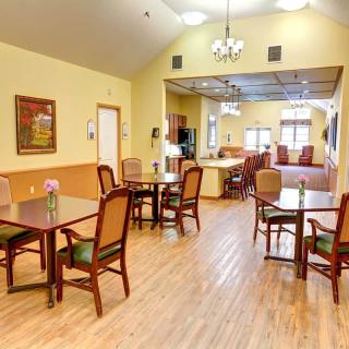A cozy dining room with wooden floors, tables, and chairs, illuminated by elegant lighting.