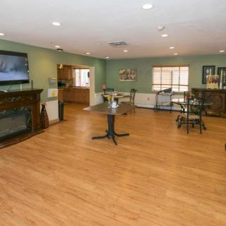 A spacious living area with wooden flooring, featuring a television, furniture, and dining tables.