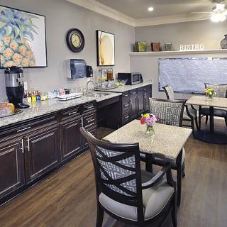 A cozy dining area with tables and chairs alongside a kitchen counter equipped with a coffee maker and decorative paintings.