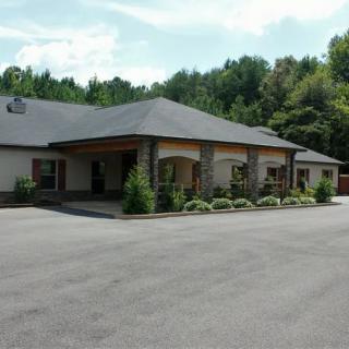 A single-story building with a parking lot in front, surrounded by trees and under a cloudy sky.