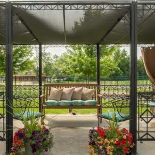 A serene outdoor gazebo with a swing, adorned with pillows and surrounded by vibrant flowers in a garden setting.