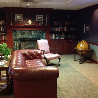 A cozy library room with a leather sofa, armchair, bookshelves, and a globe next to a fireplace.
