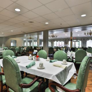 A well-arranged dining room with neatly set tables and green upholstered chairs.