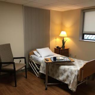 A serene hospital patient room featuring a bed, chair, and warm lighting.