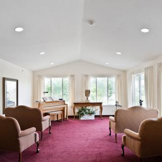A spacious living room with a red carpet, featuring elegant couches and a piano by large windows.