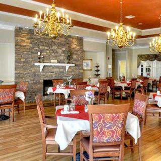 An elegant restaurant dining area featuring neatly arranged tables and chairs, chandeliers, and a stone fireplace.