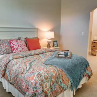 A cozy bedroom with colorful bedding and pillows, featuring a bedside lamp and a decorative tray.