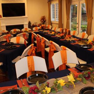 A beautifully set dining room table with fall-themed decorations in orange and black.
