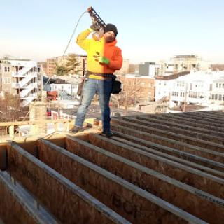 A construction worker on a roof, using a tool while wearing safety gear.