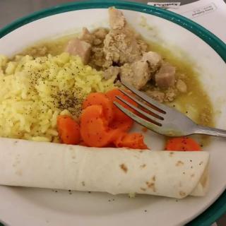 A plate of food featuring chicken, yellow rice, carrots, and a tortilla.