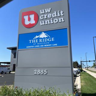 A signboard displaying UW Credit Union and The Ridge located at 2885 on a sunny day.