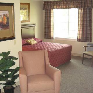A cozy bedroom with a bed, armchair, and window letting in natural light.