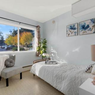A modern, minimalist bedroom with a large window letting in natural light, featuring simple decor and a touch of greenery.