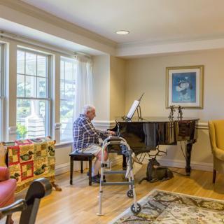 An elderly person playing the piano in a cozy living room setting.