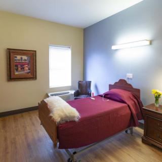 A cozy bedroom with a single bed, a window, and warm decor including a painting and flowers on the nightstand.