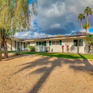 A single-story house with a well-maintained yard, featuring palm trees and a partly cloudy sky in the background.