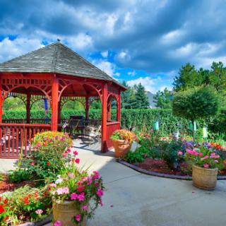 A vibrant garden featuring a charming gazebo surrounded by colorful flowers and lush greenery under a beautiful blue sky.