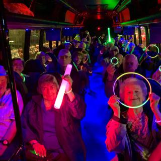 A group of seniors enjoying a lively party bus ride with glow sticks and colorful lights.
