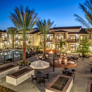 A luxurious apartment complex featuring a swimming pool and palm-lined courtyards in the evening.