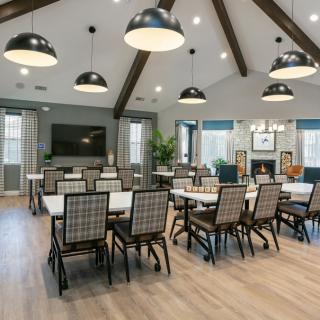 A spacious and well-lit dining or meeting area with multiple tables and chairs, featuring modern lighting fixtures and wooden ceiling beams.